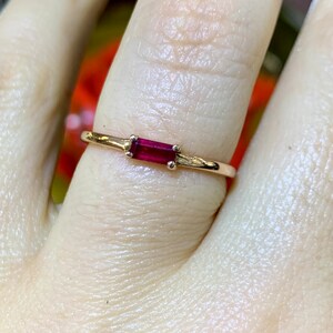 May include: A delicate gold ring with a single, rectangular, red gemstone set in the center.