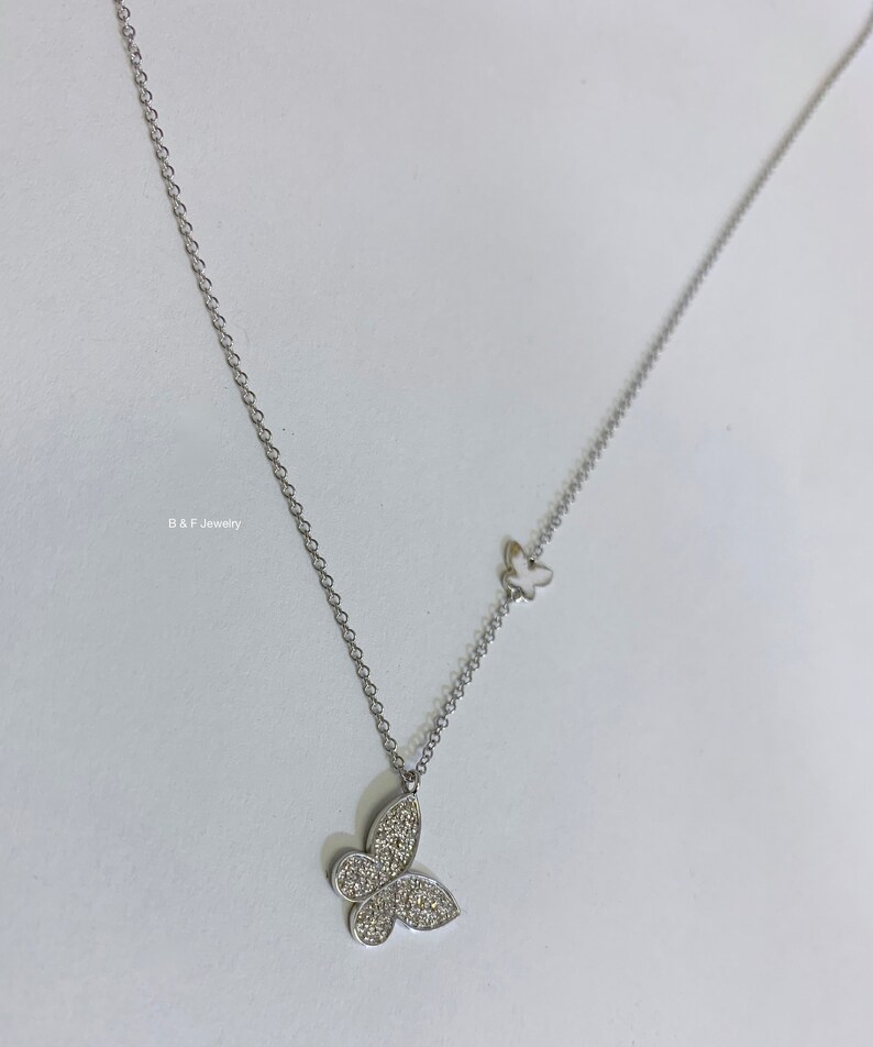 May include: A silver chain necklace with two butterfly pendants. The larger pendant is covered in small, clear stones. The smaller pendant is plain silver.