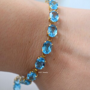 May include: A gold chain bracelet with oval-shaped blue topaz gemstones. The bracelet is on a person's wrist.