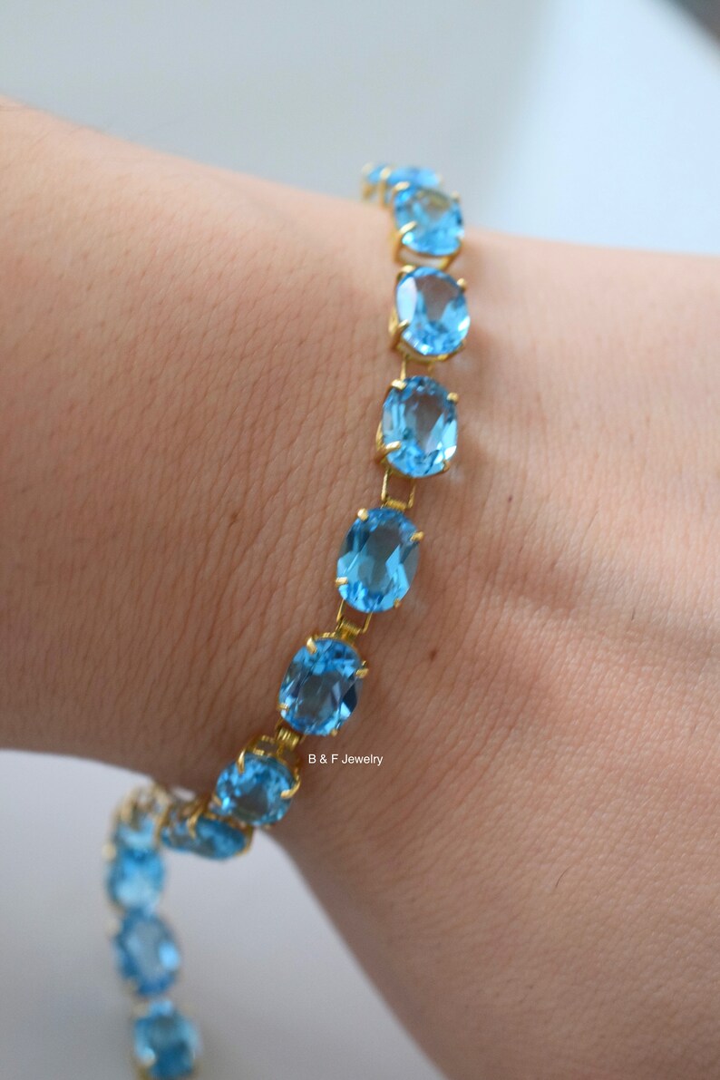 May include: A gold chain bracelet with oval-shaped blue topaz gemstones. The bracelet is on a person's wrist.