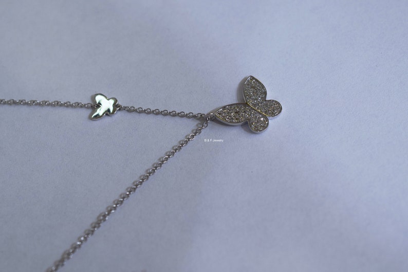 May include: A silver necklace featuring a dainty butterfly pendant. The butterfly is embellished with shimmering clear stones.