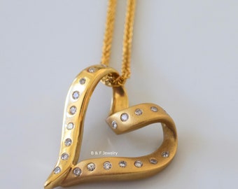 May include: Gold-toned heart pendant necklace with a delicate chain. The heart-shaped pendant is adorned with small, sparkling gemstones. The jewelry is from B & F Jewelry.