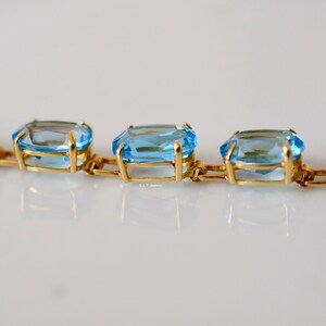 May include: A gold chain bracelet with light blue gemstones. The gemstones are rectangular and faceted.