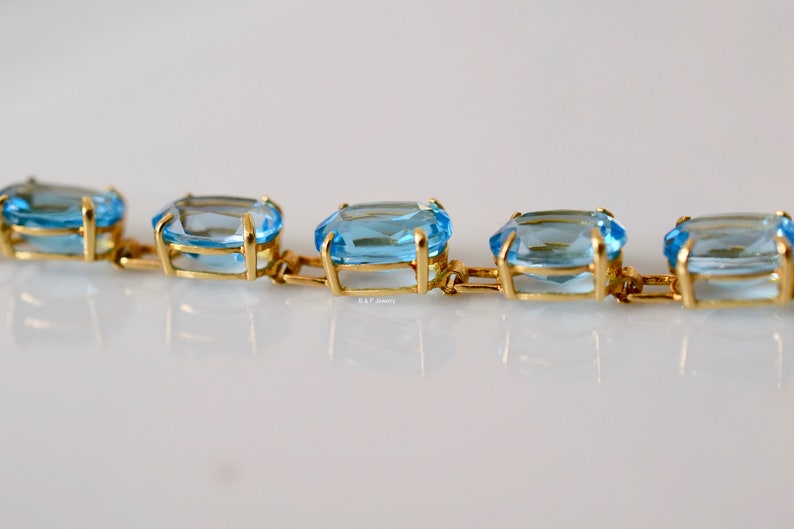May include: A gold chain bracelet with light blue gemstones. The gemstones are rectangular and faceted.