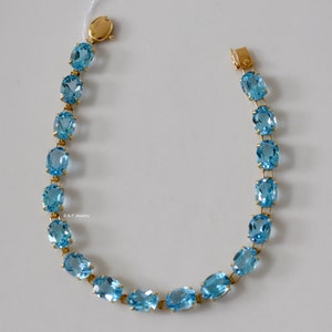 May include: A gold bracelet with a chain of oval-shaped blue topaz gemstones.