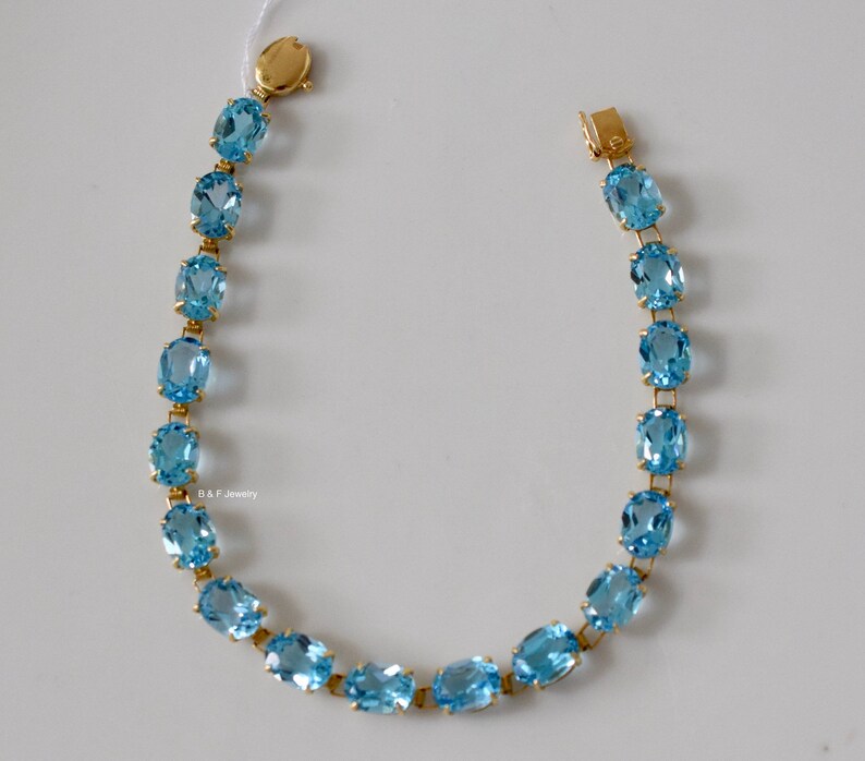 May include: A gold bracelet with a chain of oval-shaped blue topaz gemstones.