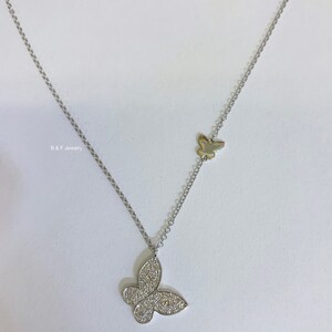 May include: A silver chain necklace with two butterfly pendants. The larger pendant is covered in small, clear stones. The smaller pendant is plain silver.