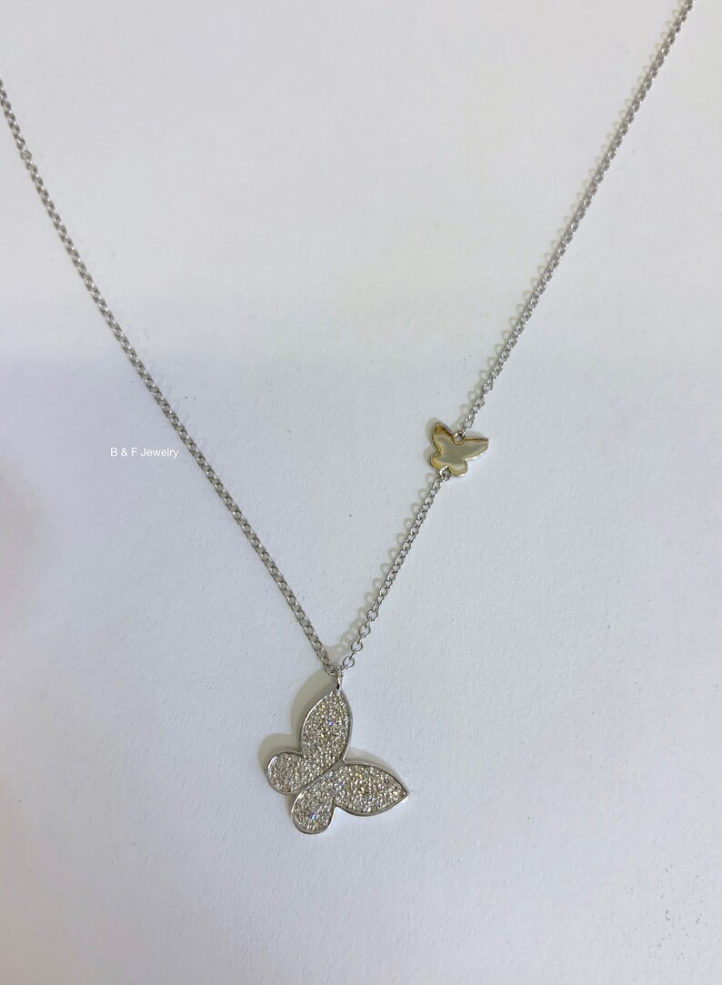 May include: A silver chain necklace with two butterfly pendants. The larger pendant is covered in small, clear stones. The smaller pendant is plain silver.