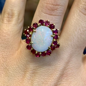 May include: A gold ring with a large white opal surrounded by a halo of small red rubies.