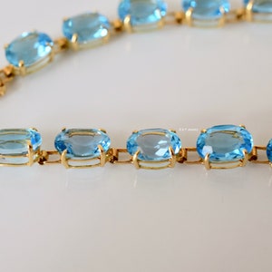 May include: A gold chain bracelet with oval-shaped blue topaz gemstones. The bracelet has a clasp closure.