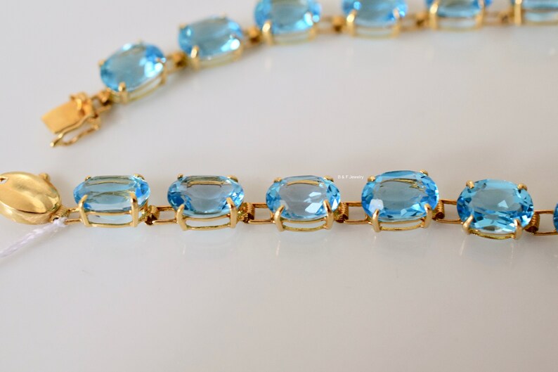 May include: A gold chain bracelet with oval-shaped blue topaz gemstones. The bracelet has a clasp closure.