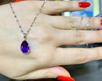 Può includere: Una collana a catena d'argento con un ciondolo a forma di pera in ametista. Il ciondolo è di colore viola scuro e ha un taglio sfaccettato.