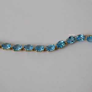 May include: A gold chain bracelet with oval-shaped blue topaz gemstones.