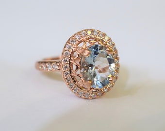 May include: A rose gold ring with a large oval aquamarine gemstone surrounded by a halo of smaller diamonds.