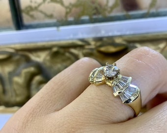 May include: A gold ring with a large round diamond in the center and smaller baguette diamonds on the band.