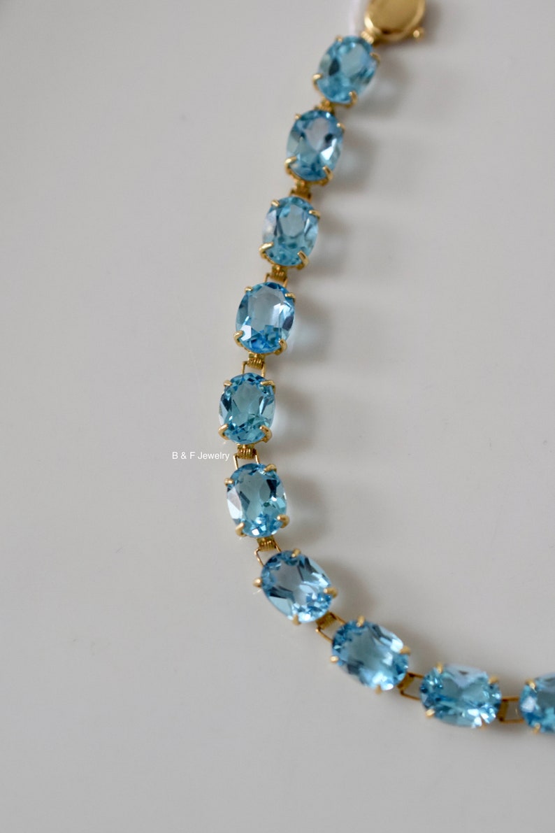 May include: A gold chain bracelet with oval-shaped blue topaz gemstones.