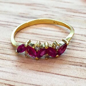 May include: A gold band ring with a row of five marquise-shaped ruby stones set in the band. The stones are accented with small round diamonds.