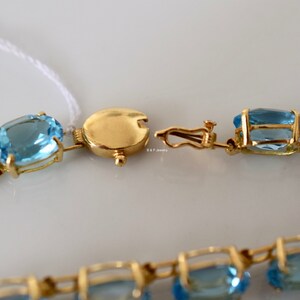 May include: A gold chain bracelet with oval-shaped blue topaz gemstones. The bracelet has a clasp closure.