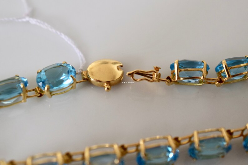 May include: A gold chain bracelet with oval-shaped blue topaz gemstones. The bracelet has a clasp closure.