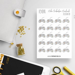 Puede incluir: Una hoja de 16 pegatinas de mandos de juego grises y blancas con un corazón rosa en cada mando. La hoja mide 8,5 cm por 12 cm. El texto "ICON Helen Rubeofon Handmade DESIGN" está en la parte superior de la hoja. El texto "SHEET SIZE 8.5 CM X 12 CM" está en la parte superior derecha de la hoja.