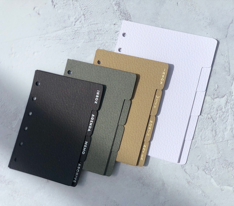 May include: Four different colored dividers for a personal planner. The dividers are black, gray, brown, and white. Each divider has a different tab with text on it. The black divider has the words "Inbox, Agenda, Memo, Archive". The gray divider has the word "Inbox". The brown divider has the words "Inbox, Week, Month, Notes". The white divider has the word "Inbox".