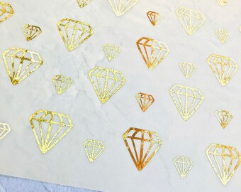 Può includere: Un foglio di carta bianca con adesivi a forma di diamante dorati con glitter. I diamanten sono di diverse dimensioni e sono disposti in modo casuale.
