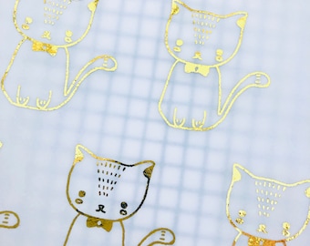 Può includere: Un foglio di carta bianca con un motivo a griglia stampato su di esso. La carta è decorata con illustrazioni di gatti in foglia d'oro che indossano papillon. I gatti sono in varie pose, alcuni seduti, alcuni in piedi e alcuni che guardano di lato.