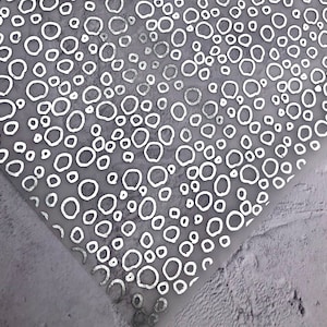 Könnte beinhalten: Weißes Geschenkpapier mit Muster und silberner Metallic-Oberfläche. Das Muster zeigt ein sich wiederholendes Design aus Kreisen und Ovalen.