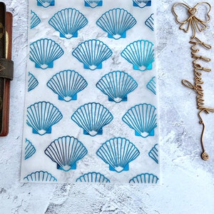 May include: A sheet of clear, translucent paper with a repeating pattern of blue seashells. The paper is designed for use in a planner or journal.