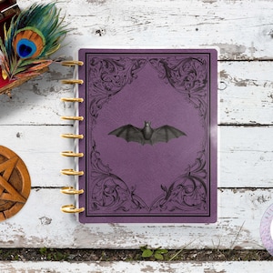 May include: Purple planner with a gold coil binding and a black bat illustration on the cover. The cover has an ornate design around the edges.