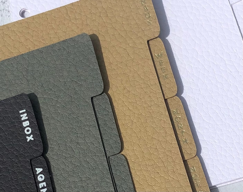 May include: Three sets of dividers for a planner or notebook. The dividers are made of textured faux leather. The top set is beige with the words "TODAY", "WEEK", "MONTH", and "NOTES". The middle set is gray with the words "INBOX" and "AGENDA". The bottom set is white.