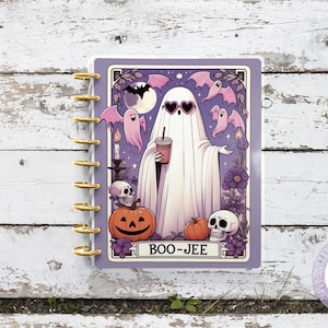Puede incluir: Una agenda morada y blanca con un fantasma sosteniendo una taza de café. El fantasma lleva gafas de sol y tiene una expresión amigable. La agenda tiene un título que dice "BOO-JEE" y presenta una calabaza, calaveras y murciélagos.