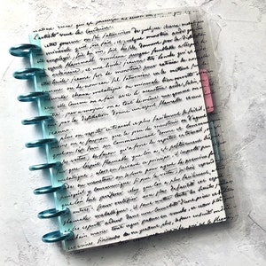 May include: A close-up of a page from a journal with handwritten text in black ink. The page is filled with cursive writing, and the text is about the process of distillation and the properties of different substances. The page is bound with a blue and clear plastic binder.
