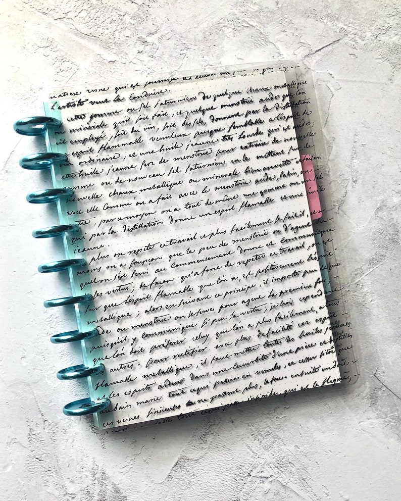 May include: A close-up of a page from a journal with handwritten text in black ink. The page is filled with cursive writing, and the text is about the process of distillation and the properties of different substances. The page is bound with a blue and clear plastic binder.