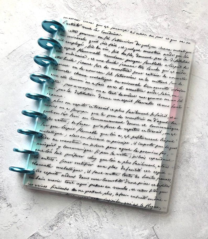 May include: A close-up of a page from a journal with handwritten notes in black ink on a light blue background. The notes discuss the process of distillation and the properties of various substances. The page is bound with a teal ring binder.