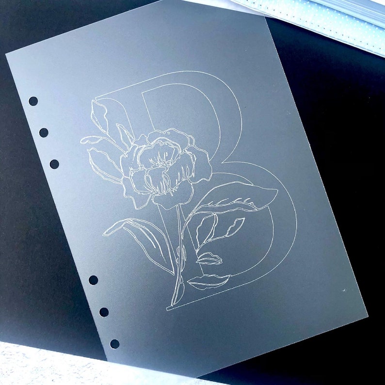 May include: A clear plastic sheet with a white outline of a flower and the letter B.