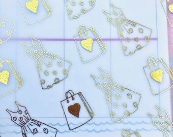 Può includere: Adesivi in ​​foglia d'oro con un motivo ripetitivo di abiti e borse della spesa. Ogni abito ha un motivo floreale e ogni borsa ha un cuore.