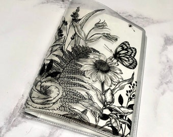 Puede incluir: Un archivador de plástico transparente con un diseño floral en blanco y negro que presenta una mariposa, helechos y flores. El diseño está impreso sobre un fondo blanco.
