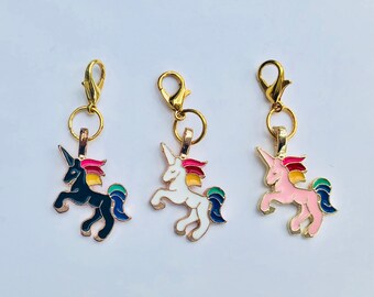 May include: Three gold unicorn charms with a rainbow mane. The unicorns are black, white, and pink.