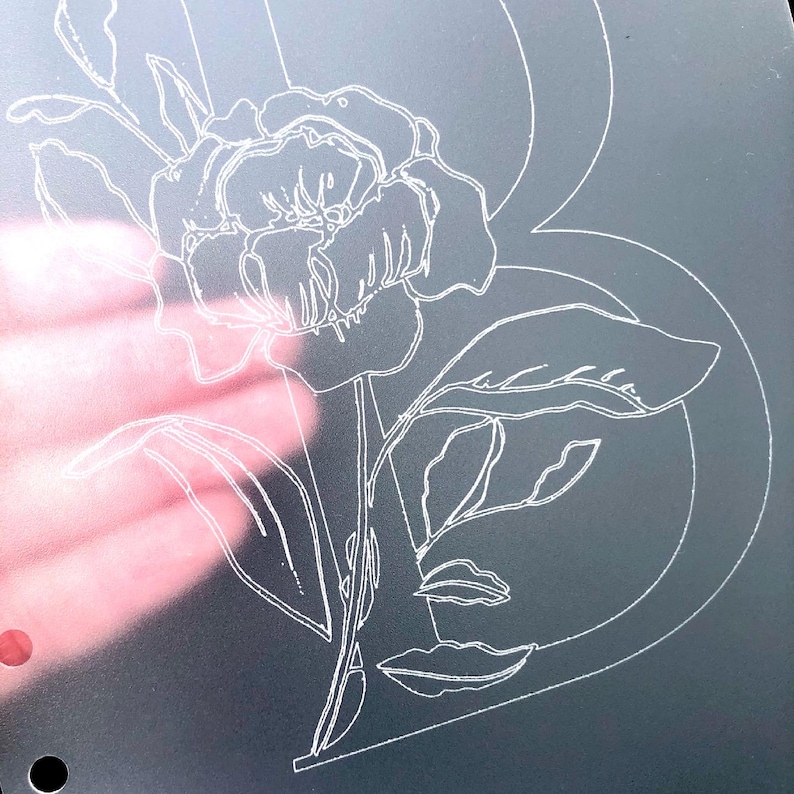 May include: A white outline of a flower with leaves on a gray background. The flower is a peony with a large center and many petals. The leaves are long and narrow.