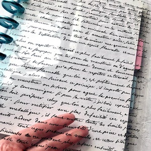 May include: A close-up of a handwritten page in a journal with black ink on white paper. The text discusses the process of distillation and the properties of different substances. The page is partially obscured by a clear plastic sheet with holes.