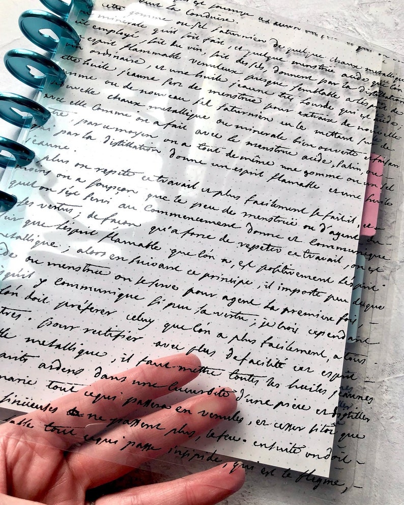May include: A close-up of a handwritten page in a journal with black ink on white paper. The text discusses the process of distillation and the properties of different substances. The page is partially obscured by a clear plastic sheet with holes.