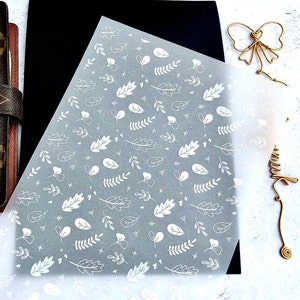 May include: A sheet of clear vellum paper with a white leaf pattern. The leaves are in various shapes and sizes, and there are small white stars scattered throughout the pattern.