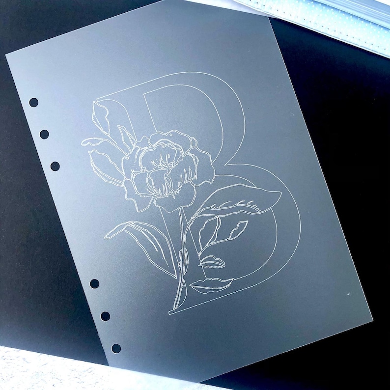 May include: A clear plastic sheet with a white outline of a flower and the letter B.