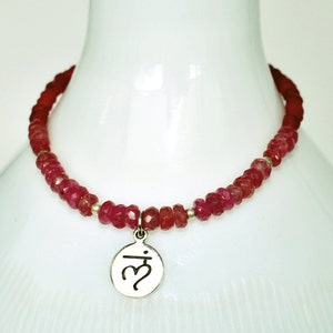 May include: A red gemstone beaded necklace with a silver charm pendant featuring the Om symbol.