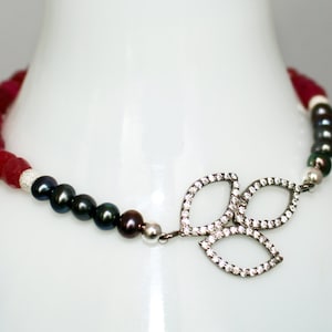 May include: A red and black beaded bracelet with a silver leaf charm. The charm is set with small clear stones.