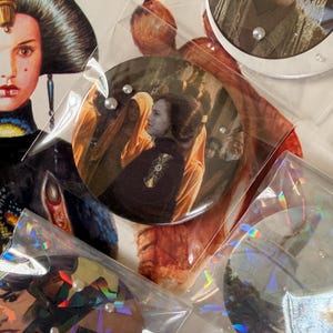 May include: Close-up of several Star Wars themed circular images and holographic stickers. The images feature characters from the movie series. Some are in clear plastic bags with small white beads. The text "PEEYOU" is visible on one sticker.