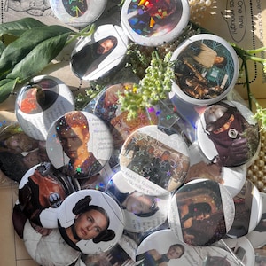 May include: A collection of round, holographic buttons featuring images of characters and scenes from a science fiction film. The buttons have a shiny, iridescent finish and are scattered on a surface with text and decorative elements.