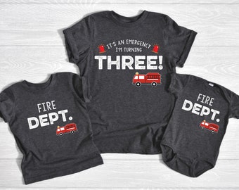 Peut inclure: Trois chemises assorties pour une famille. La plus grande chemise est gris foncé avec du texte blanc qui dit "C'est une urgence, j'ai trois ans !" avec un dessin de camion de pompiers rouge. La chemise moyenne est gris foncé avec du texte blanc qui dit "FIRE DEPT." avec un dessin de camion de pompiers rouge. La plus petite chemise est un body gris foncé avec du texte blanc qui dit "FIRE DEPT." avec un dessin de camion de pompiers rouge.