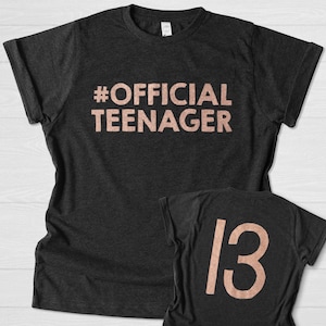 May include: A black t-shirt with the text "#OFFICIAL TEENAGER" in rose gold lettering. A second black t-shirt with the number "13" in rose gold lettering.
